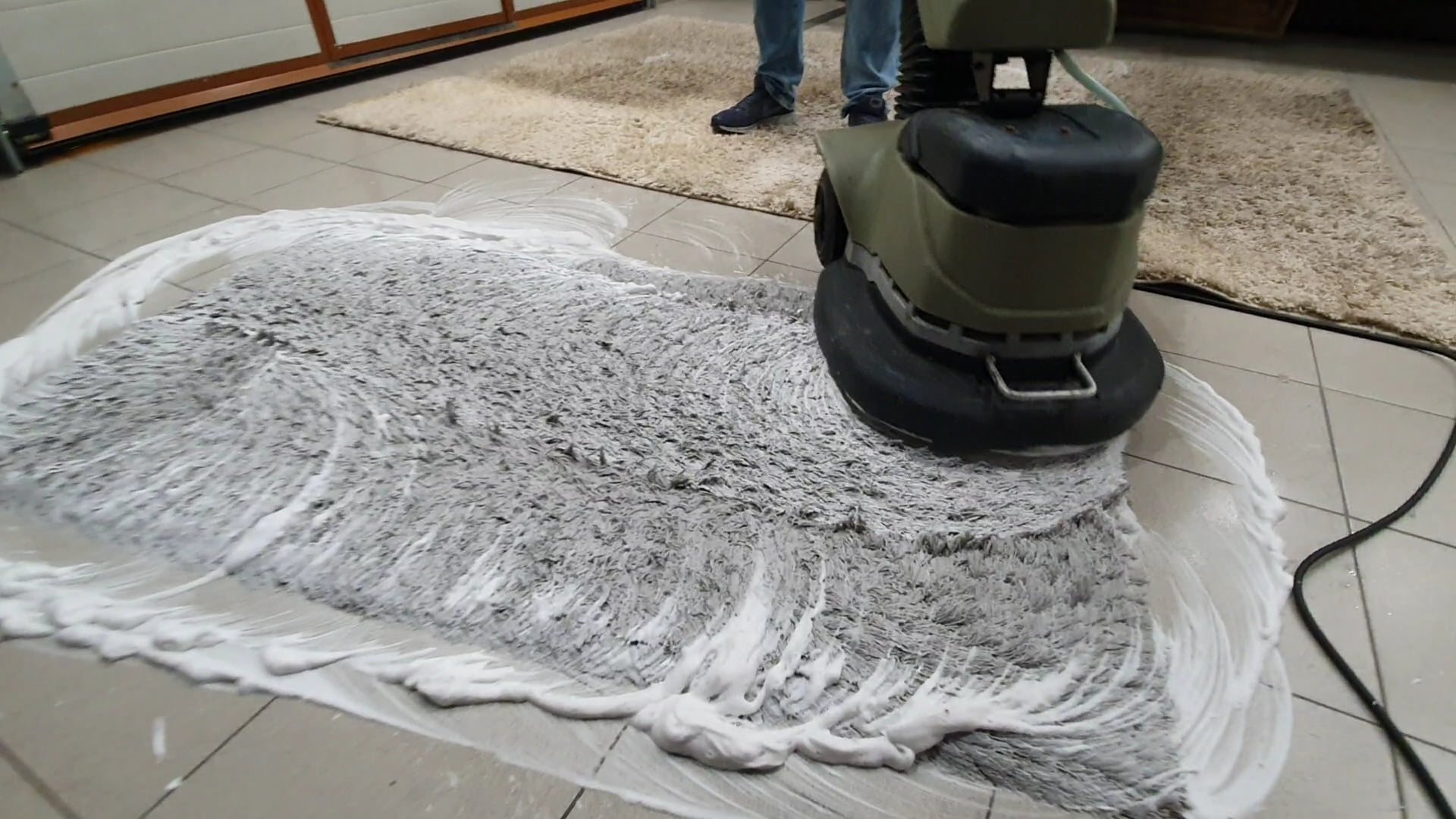 Pranie dywanu specjalistyczną maszyną przez pracownika firmy Solid Work. Widać białą pianę na czyszczonej powierzchni.