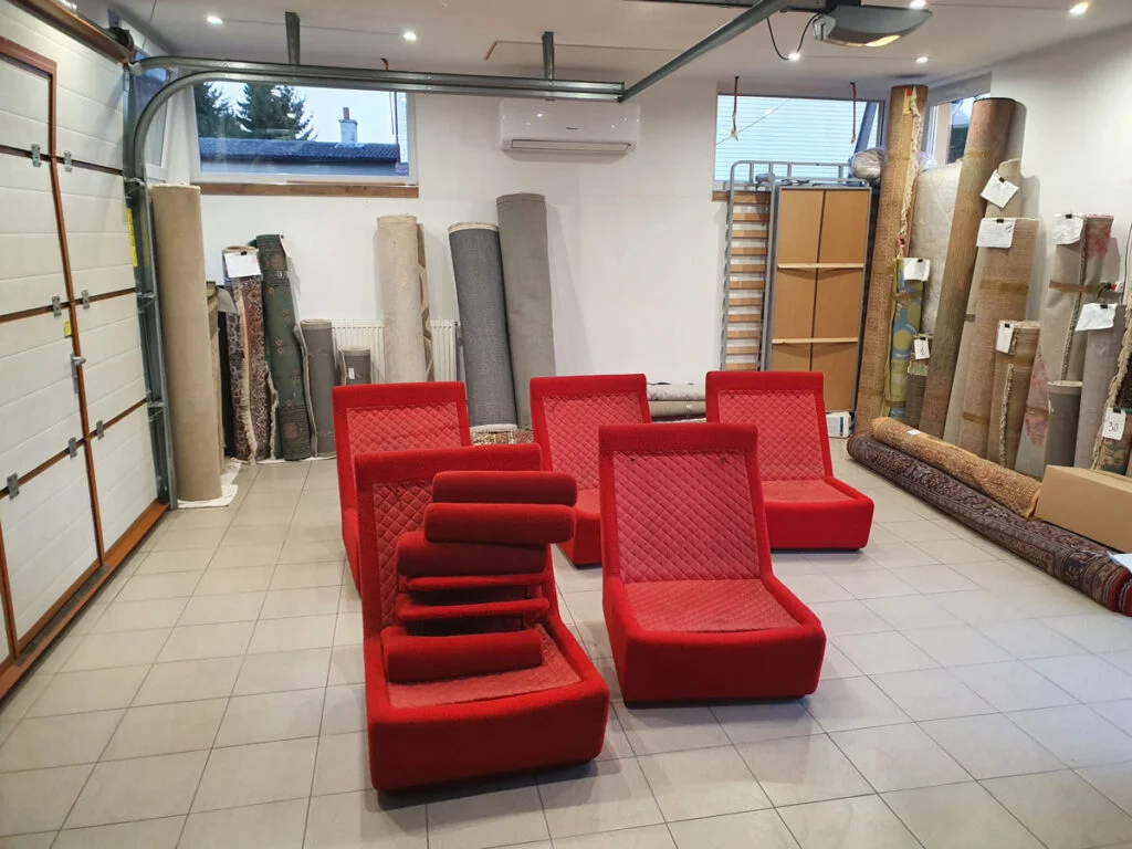 Pięć czerwonych foteli czekających na odbiór wraz z dywanami stojącymi pod ścianami pomieszczenia.
