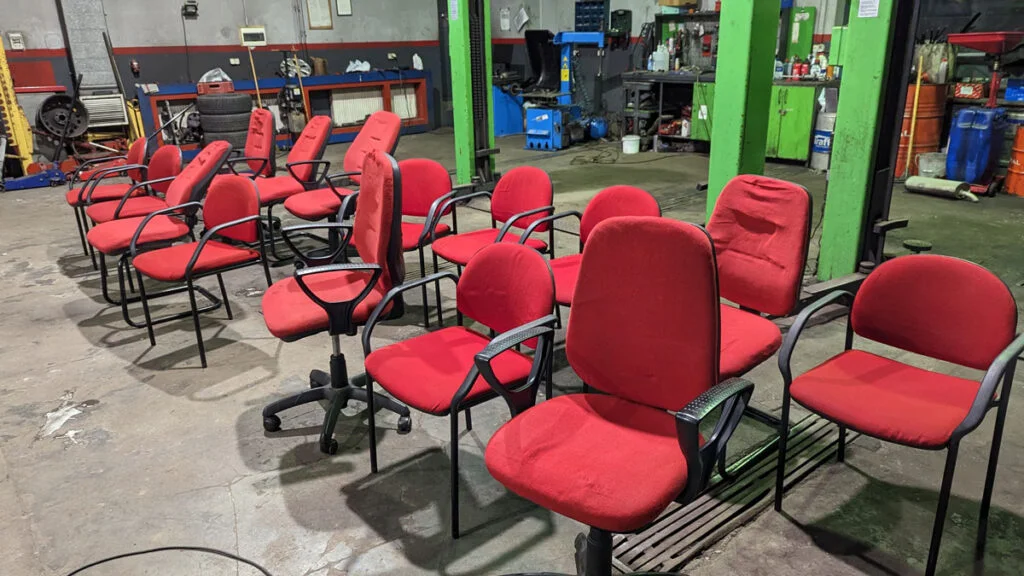 Klikanaście foteli komputerowych w czerwonymi siedziskami i oparciami zgromadzone w warsztacie samochodowym - wyprane i doczyszczone