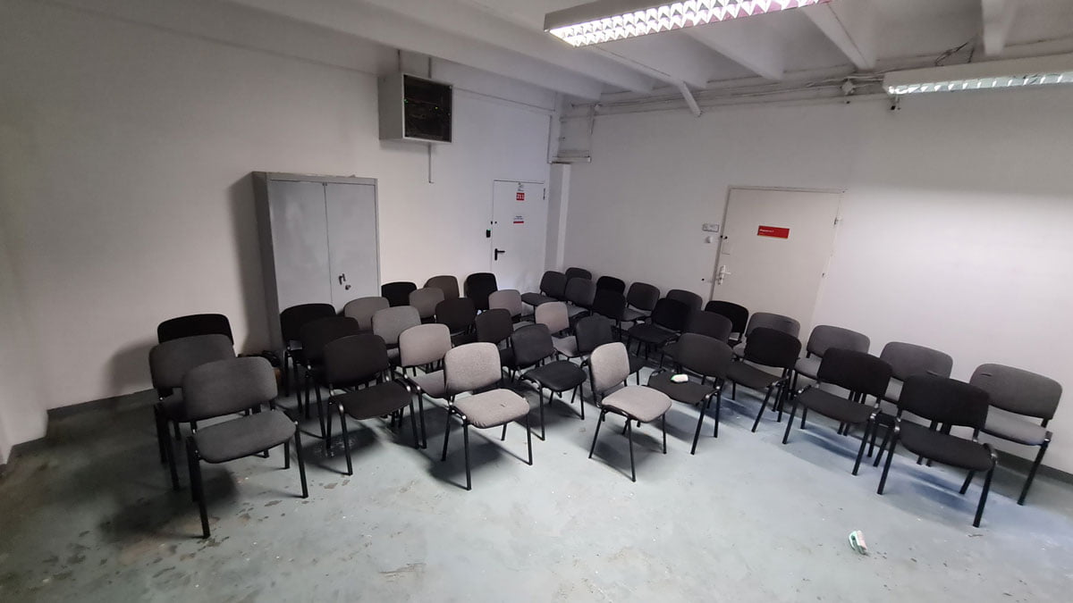 Kilkadziesiąt krzeseł szarych i czarnych zgromadzonych w pustej sali z białymi ścianami