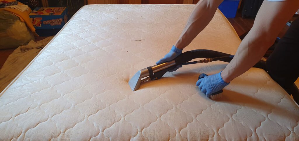 Ręce w lateksowych rękawiczkach czyszczące specjalnym odkurzaczem materac z dwuosobowego łóżka