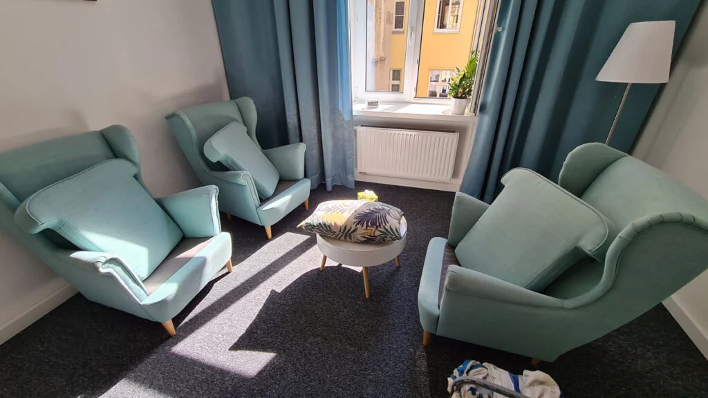Świeżo wyczyszczone trzy fotele uszaki w kolorze zielononiebieskim stojące w niewielkim salonie na czystym szarym dywanie